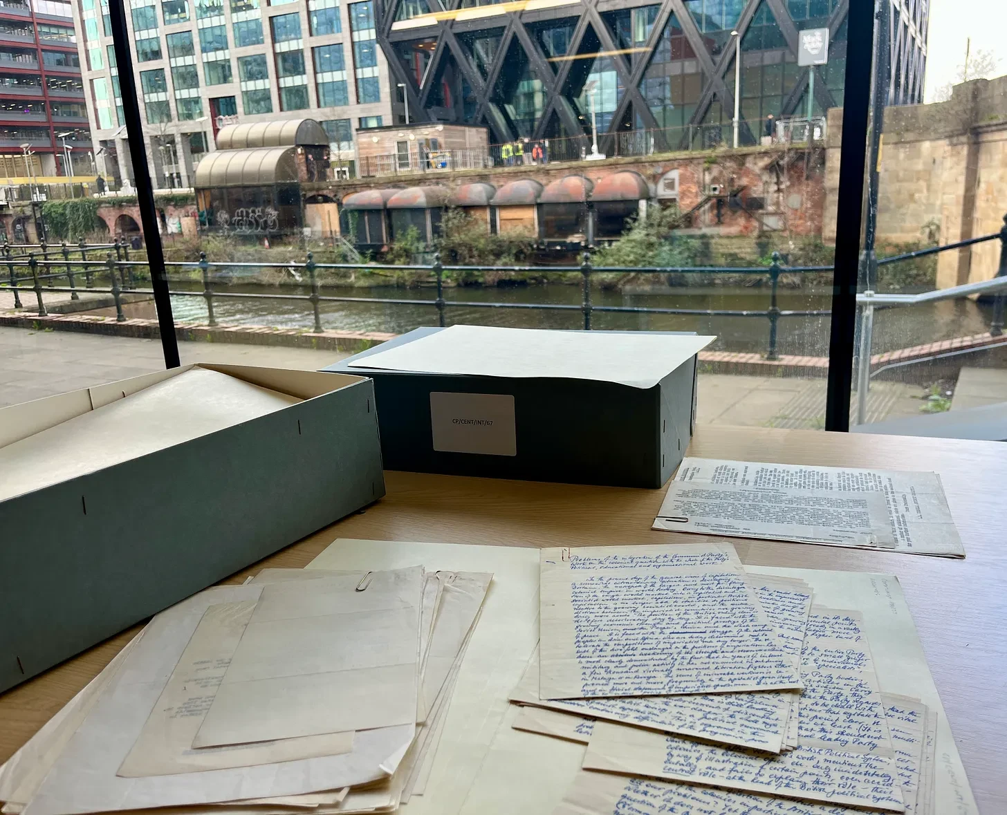 Archival documents and research materials spread on a desk overlooking a canal